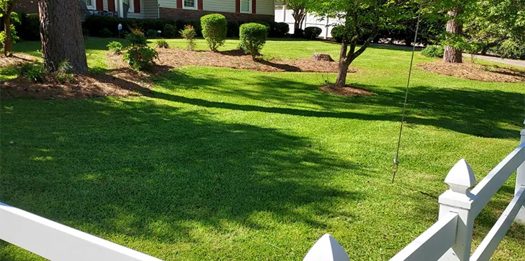 A house with a white fence and a well-maintained lawn in the foreground.